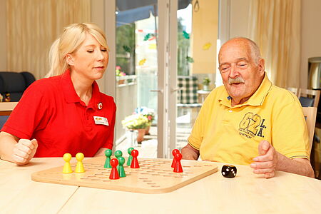 Mitarbeiterin des DRK spielt mit einem alten Herren ein Brettspiel.