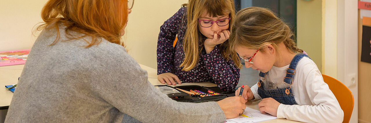Frau hilft zwei Mädchen bei Schulaufgaben.