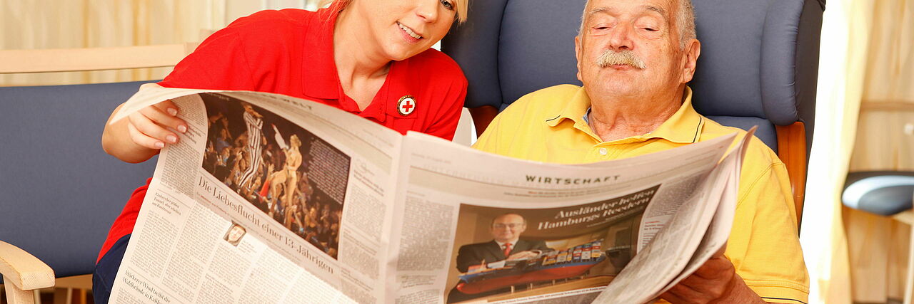 Eine Mitarbeiterin des DRK liest zusammen mit einem alten Herren die Zeitung.